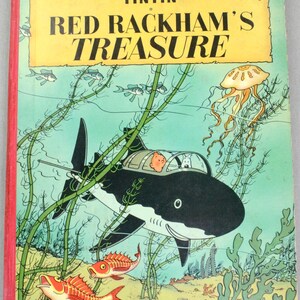 May include: A vintage copy of "Red Rackham's Treasure" by Herg&eacute;. The cover features a shark-shaped submarine with Tintin and Snowy inside, swimming underwater with fish and seaweed. The title is in large, bold letters.