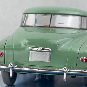 Pu&ograve; includere: Un modello di auto d'epoca verde, visto da dietro. L'auto presenta paraurti cromati, fanali posteriori rossi e un'area per la targa argentata. Il tetto dell'auto &egrave; curvo con finiture argentate.