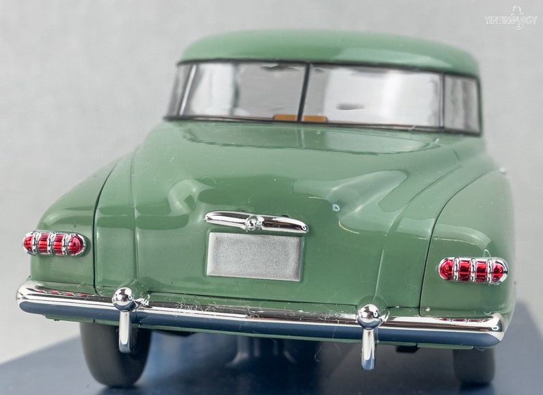 Pu&ograve; includere: Un modello di auto d'epoca verde, visto da dietro. L'auto presenta paraurti cromati, fanali posteriori rossi e un'area per la targa argentata. Il tetto dell'auto &egrave; curvo con finiture argentate.
