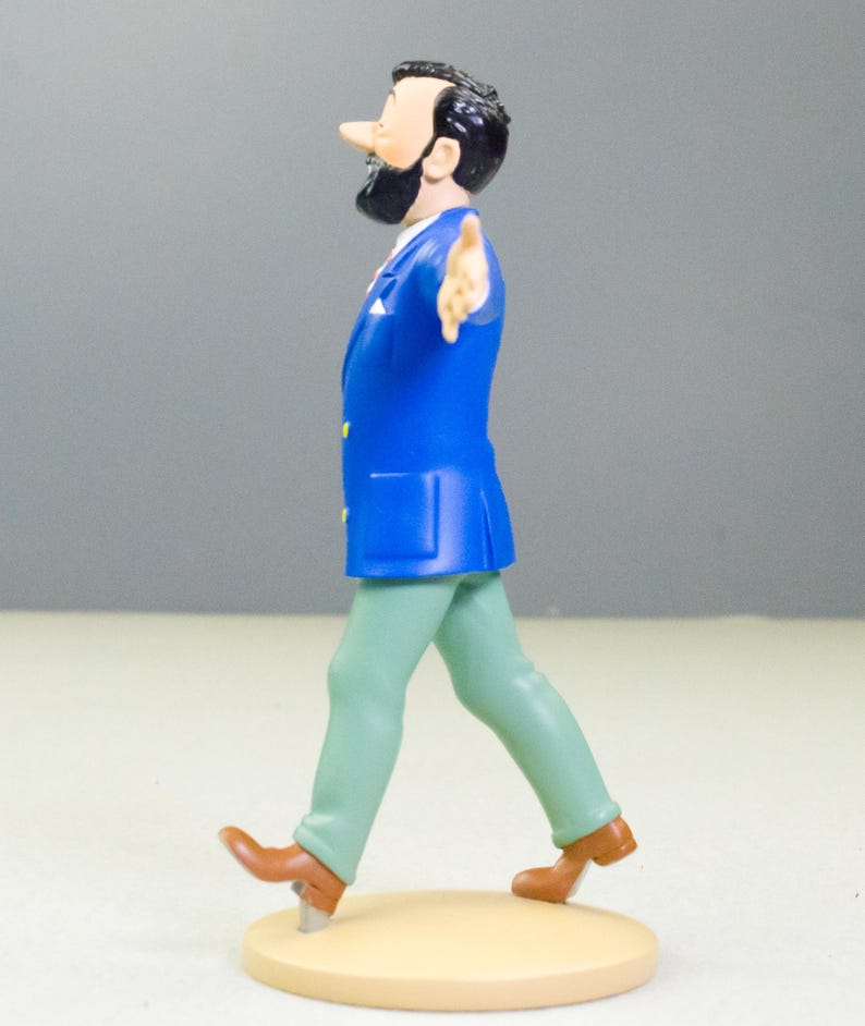 以下が含まれることがあります： 青いジャケット、緑のズボン、茶色の靴を履いた男性のフィギュア。フィギュアは黒いひげと髪を持ち、ベージュ色の台座を歩いています。フィギュアは右腕を伸ばしています。