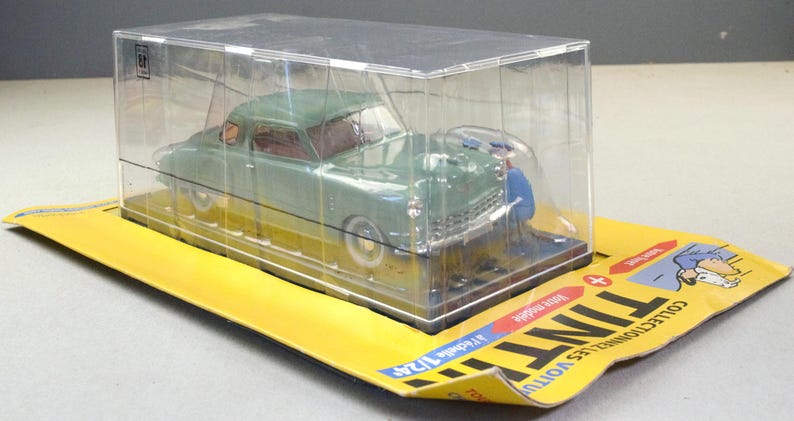 Pu&ograve; includere: Un'auto modello pressofusa verde in una vetrina trasparente, su una base di cartone gialla. L'auto misura circa 18 cm di lunghezza. La confezione presenta testo e illustrazioni in francese.
