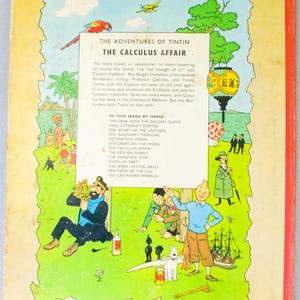 May include: The back cover of "The Adventures of Tintin: The Calculus Affair" comic book. The cover features colorful illustrations of Tintin, Captain Haddock, and other characters. The book's title and series are displayed at the top.