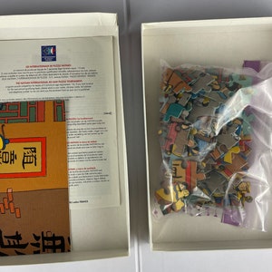 Peut inclure: Une bo&icirc;te blanche contenant un puzzle. Les pi&egrave;ces du puzzle sont color&eacute;es et repr&eacute;sentent une sc&egrave;ne de dessin anim&eacute;. La bo&icirc;te contient &eacute;galement un petit livret avec des instructions et une image du puzzle termin&eacute;.