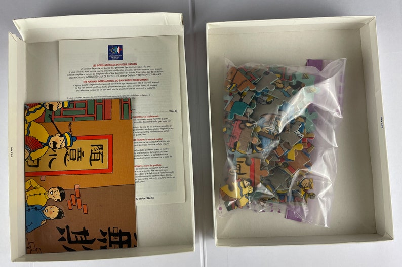Peut inclure: Une bo&icirc;te blanche contenant un puzzle. Les pi&egrave;ces du puzzle sont color&eacute;es et repr&eacute;sentent une sc&egrave;ne de dessin anim&eacute;. La bo&icirc;te contient &eacute;galement un petit livret avec des instructions et une image du puzzle termin&eacute;.