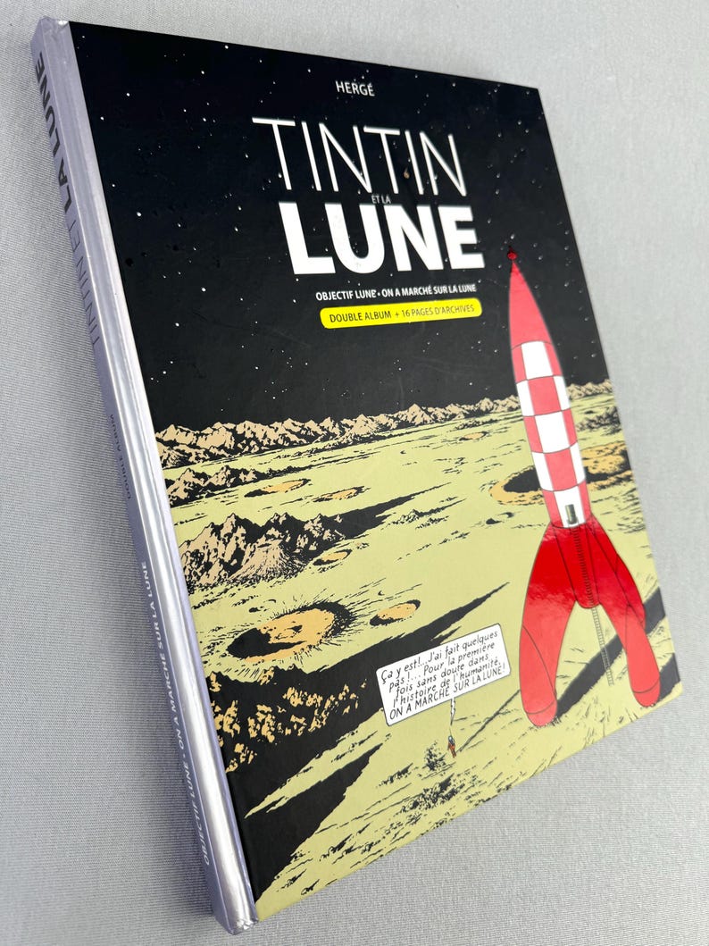 Puede incluir: Un c&oacute;mic titulado "Tint&iacute;n y la Luna" con una ilustraci&oacute;n de un cohete rojo y blanco contra un cielo estrellado negro. La portada tambi&eacute;n presenta un paisaje lunar en tonos amarillos y marrones.