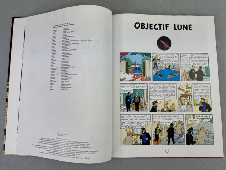 Puede incluir: Libro abierto con el t&iacute;tulo "OBJECTIF LUNE" e ilustraciones de c&oacute;mic. La p&aacute;gina izquierda contiene texto. La p&aacute;gina derecha presenta una tira c&oacute;mica con un cohete y un coche azul.