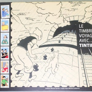 May include: A hardcover book with a red spine and a black and white illustration of Tintin and Snowy. The book's title, "LE TIMBRE VOYAGE AVEC... TINTIN," is displayed prominently. The cover also features a series of stamp-like images.