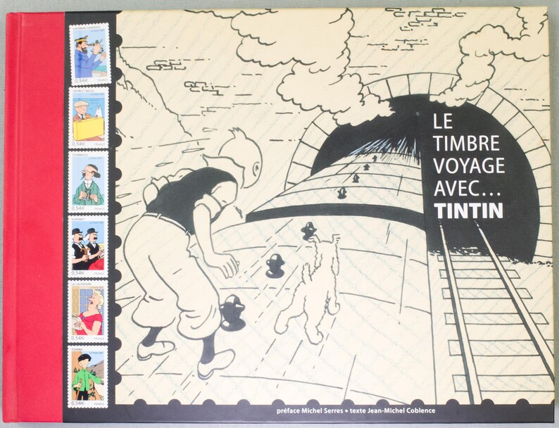 May include: A hardcover book with a red spine and a black and white illustration of Tintin and Snowy. The book's title, "LE TIMBRE VOYAGE AVEC... TINTIN," is displayed prominently. The cover also features a series of stamp-like images.