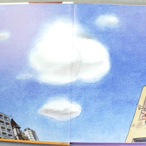K&ouml;nnte beinhalten: Eine Buchseite mit einem blauen Himmel und wei&szlig;en Wolken. Links ist eine Ansammlung von Stadtgeb&auml;uden zu sehen. Rechts zeigt ein helles Geb&auml;ude eine Zeichentrickfigur mit gelben Haaren, die aus einem Fenster heraus in den Himmel zeigt.