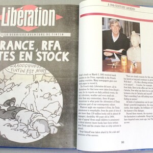 Puede incluir: Un libro abierto con una cubierta azul. La p&aacute;gina izquierda presenta el peri&oacute;dico franc&eacute;s "Lib&eacute;ration" con el titular "FRANCE, RFA VOTES EN STOCK" y un dibujo de Tint&iacute;n. La p&aacute;gina derecha muestra una foto de un hombre con un avi&oacute;n en miniatura.