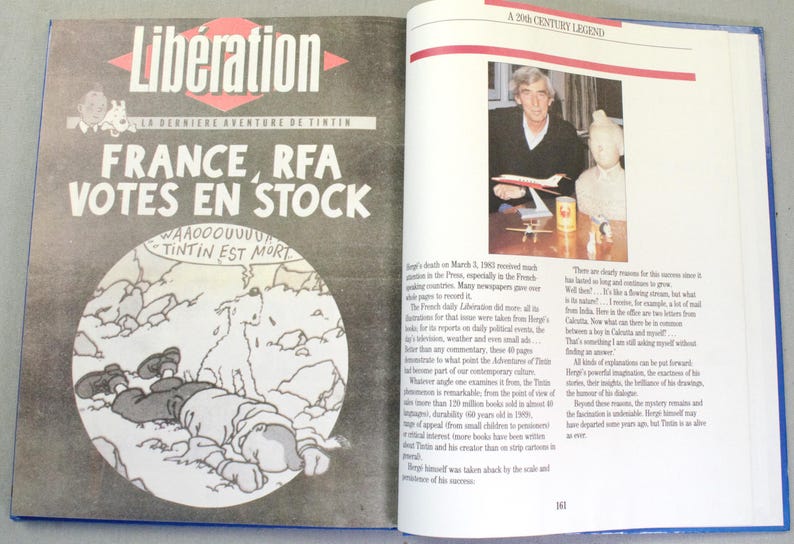 Puede incluir: Un libro abierto con una cubierta azul. La p&aacute;gina izquierda presenta el peri&oacute;dico franc&eacute;s "Lib&eacute;ration" con el titular "FRANCE, RFA VOTES EN STOCK" y un dibujo de Tint&iacute;n. La p&aacute;gina derecha muestra una foto de un hombre con un avi&oacute;n en miniatura.