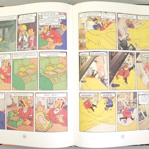 May include: Open book with comic strip panels. The panels depict cartoon characters in various scenes, including a man in a red suit, a man in a blue uniform, and other figures. Speech bubbles contain text.