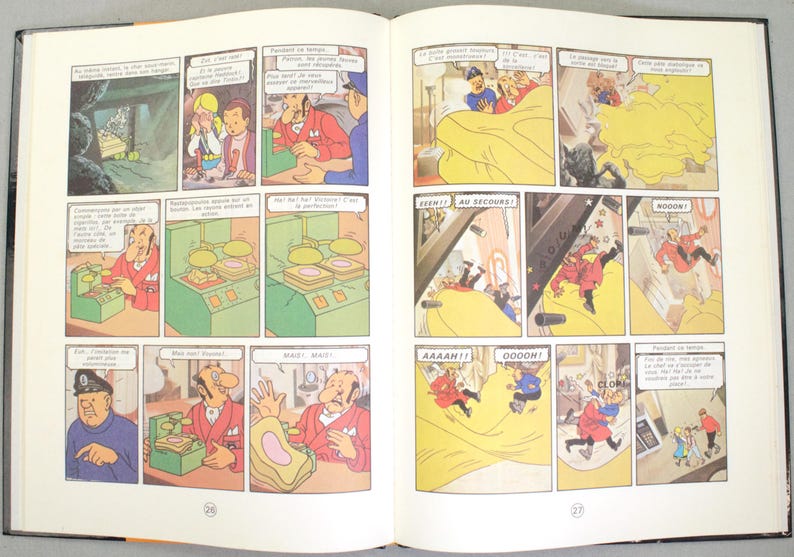 May include: Open book with comic strip panels. The panels depict cartoon characters in various scenes, including a man in a red suit, a man in a blue uniform, and other figures. Speech bubbles contain text.