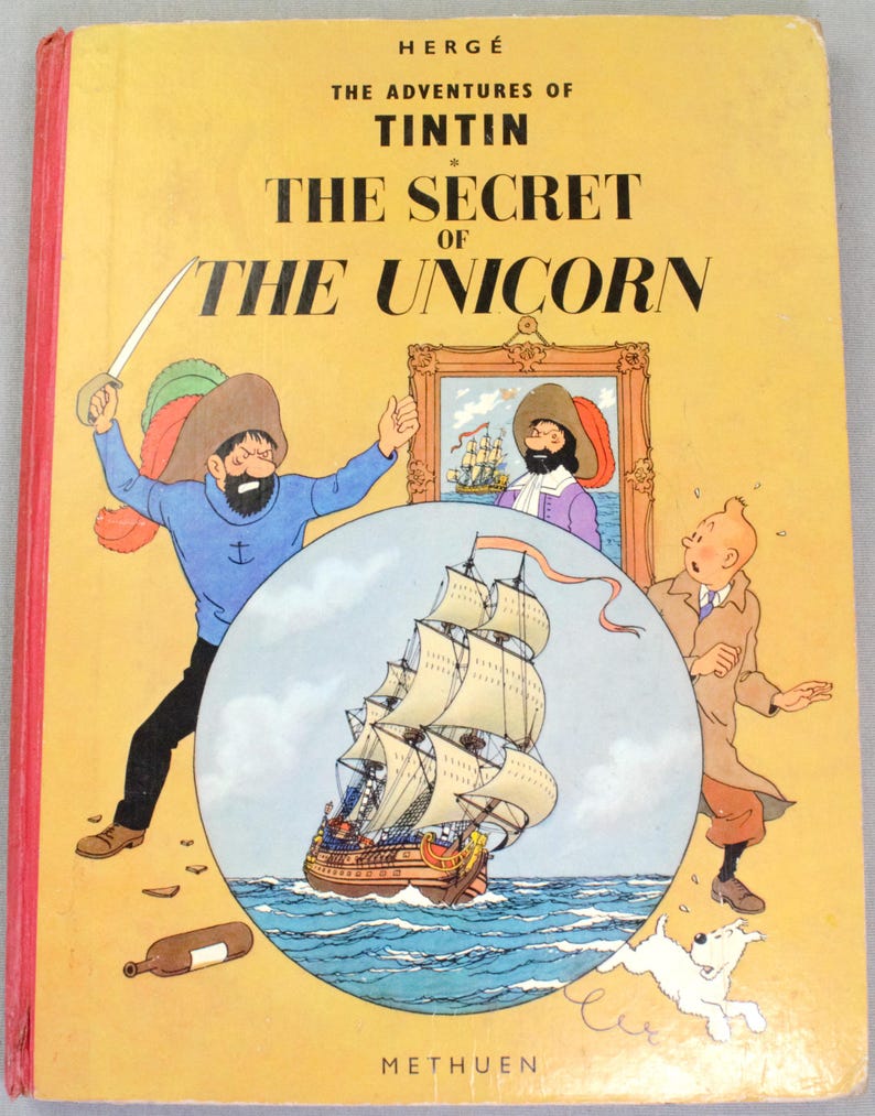 May include: A vintage hardcover book titled "The Adventures of Tintin: The Secret of the Unicorn" by Herg&eacute;. The cover features illustrations of Captain Haddock, Tintin, a ship, and Snowy the dog, with a yellow background.