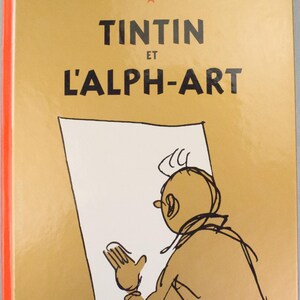 Może przedstawiać: Okładka książki "Tintin et l'Alph-Art" autorstwa Herg&eacute;. Okładka jest w jasnobrązowym kolorze z tytułem dużymi czarnymi literami. Czerwona gwiazda znajduje się nad tytułem. Ilustracja Tintina znajduje się na okładce, trzymającego rysunek.