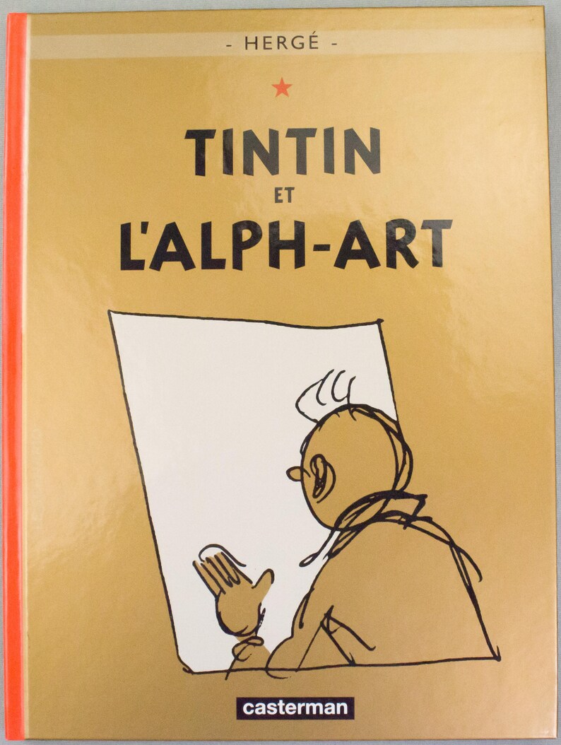 Może przedstawiać: Okładka książki "Tintin et l'Alph-Art" autorstwa Herg&eacute;. Okładka jest w jasnobrązowym kolorze z tytułem dużymi czarnymi literami. Czerwona gwiazda znajduje się nad tytułem. Ilustracja Tintina znajduje się na okładce, trzymającego rysunek.