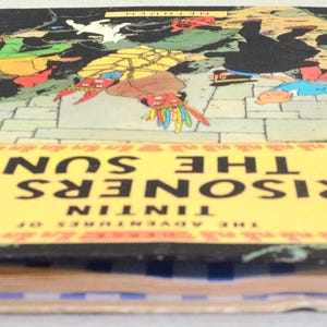 Op de afbeelding: Een vintage hardcover boek getiteld "Tintin: De Zonnetempel". De omslag toont een kleurrijke illustratie van personages in een avontuurlijke sc&egrave;ne tegen een donkere achtergrond. Het boek heeft een gele titelbanner en een rode rug.