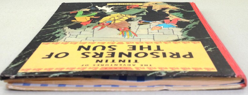 Op de afbeelding: Een vintage hardcover boek getiteld "Tintin: De Zonnetempel". De omslag toont een kleurrijke illustratie van personages in een avontuurlijke sc&egrave;ne tegen een donkere achtergrond. Het boek heeft een gele titelbanner en een rode rug.