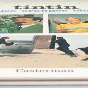 Puede incluir: Un libro antiguo de tapa dura titulado "Tint&iacute;n et les oranges bleues" con lomo azul. La portada presenta cuatro paneles con ilustraciones de personajes y escenas de la historia. El nombre del editor, Casterman, est&aacute; impreso en la parte inferior.