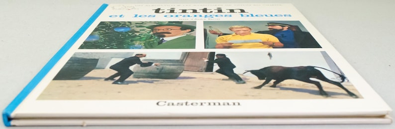 Puede incluir: Un libro antiguo de tapa dura titulado "Tint&iacute;n et les oranges bleues" con lomo azul. La portada presenta cuatro paneles con ilustraciones de personajes y escenas de la historia. El nombre del editor, Casterman, est&aacute; impreso en la parte inferior.