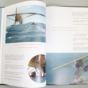 May include: An open book featuring illustrations of a seaplane landing in the sea. The text reads "TOUCHE EN PLEIN VOL, LE CN-1411 A AMERRI DANS UNE BRUTALE GERBE D'EAU". The book is open to two pages with images and text.