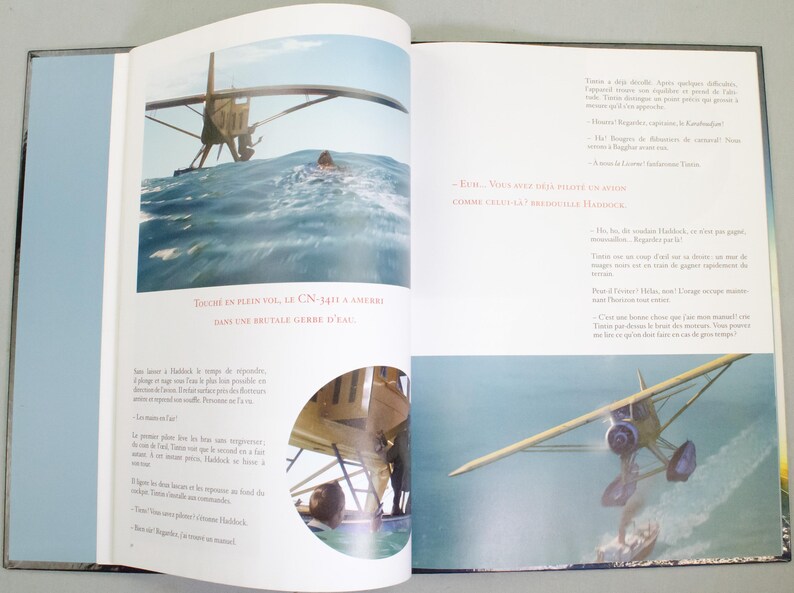 May include: An open book featuring illustrations of a seaplane landing in the sea. The text reads "TOUCHE EN PLEIN VOL, LE CN-1411 A AMERRI DANS UNE BRUTALE GERBE D'EAU". The book is open to two pages with images and text.