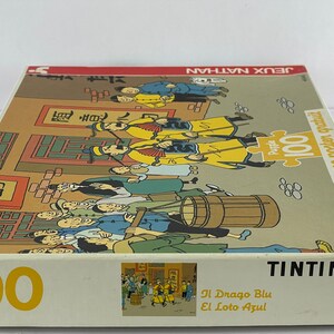Peut inclure: Un puzzle de 100 pi&egrave;ces repr&eacute;sentant une sc&egrave;ne de la bande dessin&eacute;e de Tintin "Le Lotus Bleu". La bo&icirc;te du puzzle montre Tintin et son chien Milou dans une rue chinoise bond&eacute;e.