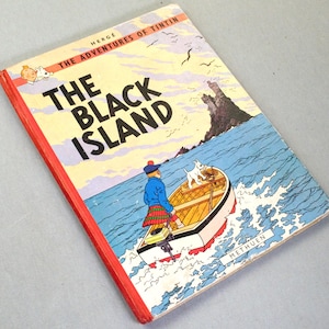 K&ouml;nnte beinhalten: Ein Vintage-Exemplar von Herg&eacute;s "Die Schwarze Insel". Das Cover zeigt Tim und Struppi in einem Boot, mit einer K&uuml;stenszene und einer Burg. Das Buch hat einen roten Buchr&uuml;cken.