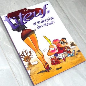 K&ouml;nnte beinhalten: Ein Titeuf-Comicbuch mit dem Titel Titeuf 5 et le derri&egrave;re des choses von Zep. Das Cover zeigt eine farbenfrohe Cartoon-Illustration einer Person mit langen Beinen in Rock und High Heels sowie zwei jungen Charakteren mit Rucks&auml;cken.