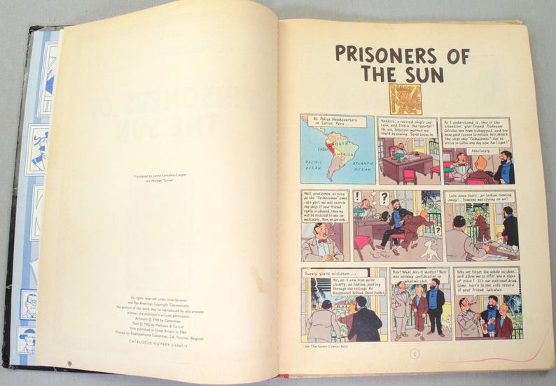 Op de afbeelding: Open boek met de titel "Prisoners of the Sun". De pagina's tonen stripverhalen met illustraties en tekst. Een kaart van Zuid-Amerika is ook zichtbaar.