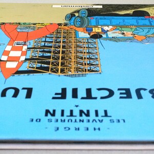 K&ouml;nnte beinhalten: Ein Hardcover-Buch mit dem Titel "OBJECTIF LUNE" von Herg&eacute;, mit einer Rakete und einer Startstruktur auf dem Cover. Das Cover ist &uuml;berwiegend blau mit gelben R&auml;ndern und dem Titel in Wei&szlig;. Das Buch ist ein Comic.