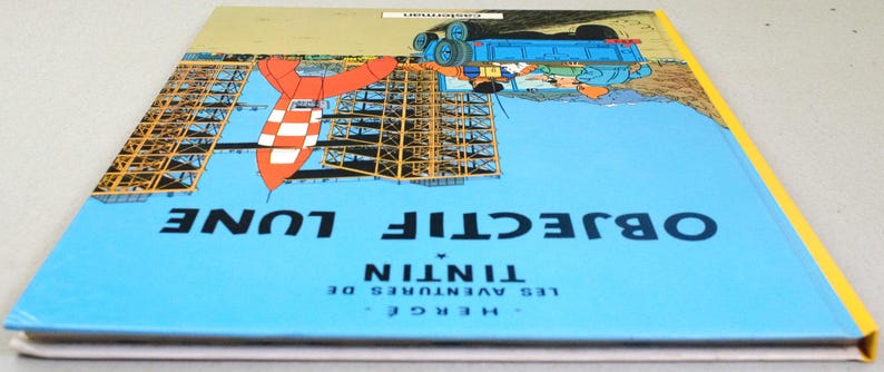 K&ouml;nnte beinhalten: Ein Hardcover-Buch mit dem Titel "OBJECTIF LUNE" von Herg&eacute;, mit einer Rakete und einer Startstruktur auf dem Cover. Das Cover ist &uuml;berwiegend blau mit gelben R&auml;ndern und dem Titel in Wei&szlig;. Das Buch ist ein Comic.