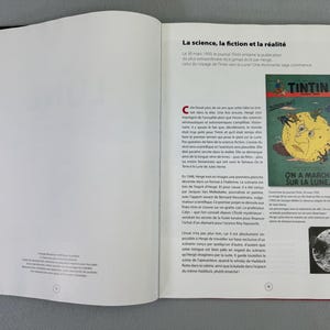 Puede incluir: Libro abierto con lomo rojo y cubierta negra. La p&aacute;gina de la derecha presenta texto en franc&eacute;s y una ilustraci&oacute;n de la portada del c&oacute;mic de Tint&iacute;n titulado "On a march&eacute; sur la Lune".