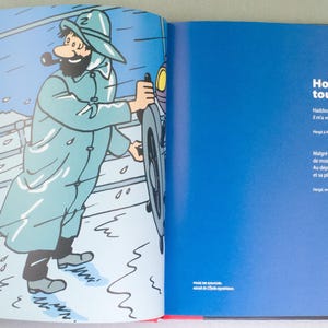 May include: A double-page spread from a comic book featuring a cartoon illustration. The left page shows a man in a blue coat and hat, holding a wheel, with a dog and another person. The right page has blue background with white text.