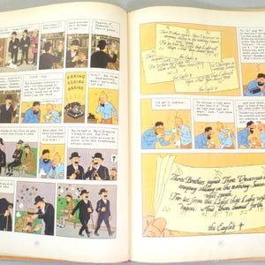 May include: Open book with comic strip panels featuring illustrations of characters in suits and hats. Text bubbles and handwritten notes are present. The comic strip has a vintage style with a yellowed background.