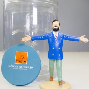 以下が含まれることがあります： タンタンシリーズのハドック船長のフィギュア。 金色のボタンが付いた青いブレザー、緑色のズボン、茶色の靴を履いています。 フィギュアの高さは約12cmで、ベージュ色の台座の上に立っています。 タンタンのロゴが入った青い丸いタグも付いています。