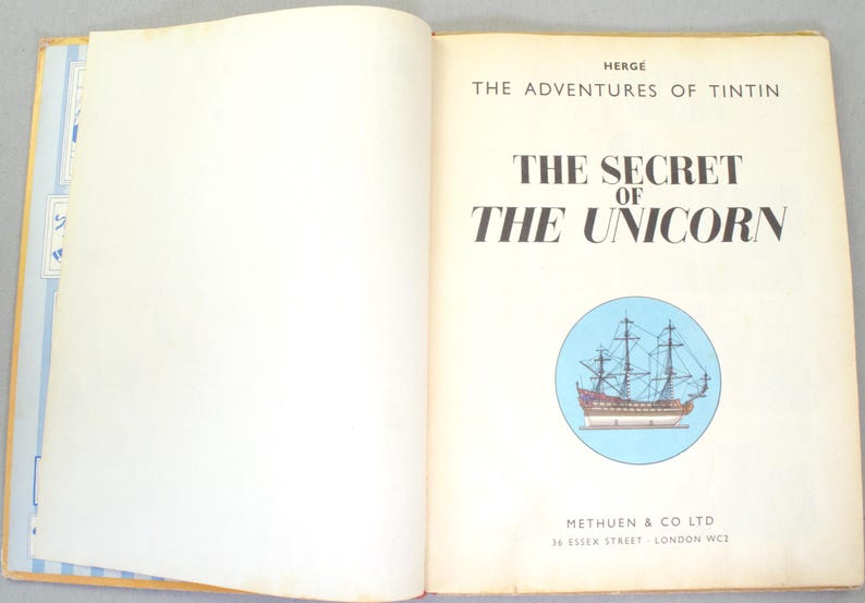 May include: Open book with the title "The Secret of the Unicorn" by Herg&eacute;. The book features a blue circle with a ship illustration. The publisher's name and address are at the bottom.