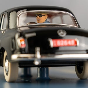 Puede incluir: Un modelo de coche Mercedes-Benz negro vintage con neum&aacute;ticos de banda blanca. El coche tiene una matr&iacute;cula roja y una figura de un conductor con gafas. Un coche cl&aacute;sico de colecci&oacute;n.