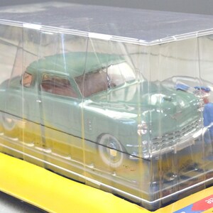 Pu&ograve; includere: Un modello di auto d'epoca verde menta in una vetrina di plastica trasparente. Il modello ha pneumatici a fascia bianca e dettagli cromati. Una piccola figura in tuta blu &egrave; posizionata vicino all'auto. L'auto &egrave; su una base gialla.