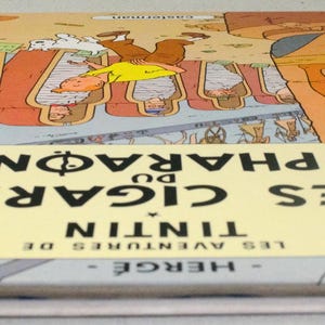 Pode incluir: Um livro de capa dura intitulado "Les Cigares du Pharaon" de Herg&eacute;. A capa apresenta ilustra&ccedil;&otilde;es eg&iacute;pcias e uma faixa amarela central com o t&iacute;tulo. O livro tem uma lombada azul e est&aacute; em bom estado.