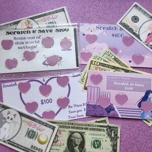 May include: A pink and purple scratch-off card with the text "Scratch & Save $100". The card has several pink hearts on it. There are also several $100 bills in the image.
