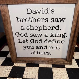 May include: Wooden framed sign with the text "David's brothers saw a shepherd. God saw a king. Let God define you and not others." The sign has a white background and a brown wooden frame.
