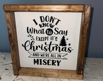 May include: A wooden framed sign with the text "I DON'T KNOW What to Say EXCEPT IT'S Christmas AND WE'RE ALL IN MISERY" in black lettering on a white background. The frame is made of stained wood.