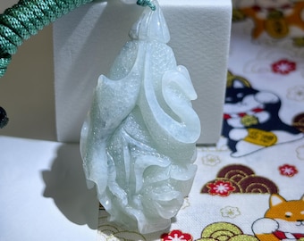 May include: A light green jade pendant carved in a flowing, organic design. The pendant is suspended from a green braided cord with a small bead. The jade has a translucent quality, and the carving features intricate details.