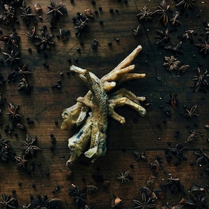 May include: A close-up of chicken feet on a wooden surface with star anise and peppercorns scattered around. The chicken feet are light brown and appear to be cooked.