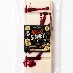 Pode incluir: Derretimentos de cera de soja em embalagem plástica transparente. As barras de cera retangulares, esbranquiçadas, têm gotas vermelho-escuras que se assemelham a sangue. O rótulo diz "HELLO, SIDNEY" com o texto "SCREAM" e "Black Pepper, Sandalwood".