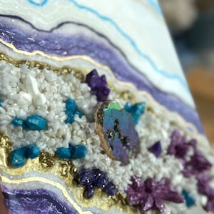 Op de afbeelding: Een vierkant kunstharswerk met een witte achtergrond en een agaatontwerp in paars, blauw en goud. De agaat is gevuld met kleine witte, blauwe en paarse kristallen.