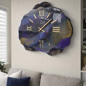 May include: A large, wall-mounted clock with an irregular, organic shape. The clock face has a swirling pattern of blue, purple, and gold resin. Gold Roman numerals and hands are featured. A decorative home accent.