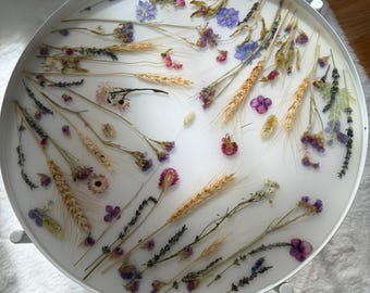 May include: A white round tray with dried flowers and wheat stalks embedded in clear resin. The flowers are shades of purple, pink, and white.
