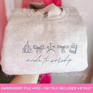 May include: Light gray sweatshirt with embroidered religious symbols, including a church, bows, crosses, and a Bible. The phrase "made to worship" is embroidered below the symbols. The sweatshirt measures 8" x 3.5".